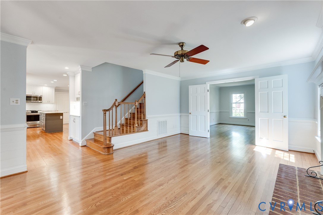 Hardwood flooring throughout, a traditional wooden staircase, white paneled doors, and a ceiling fan