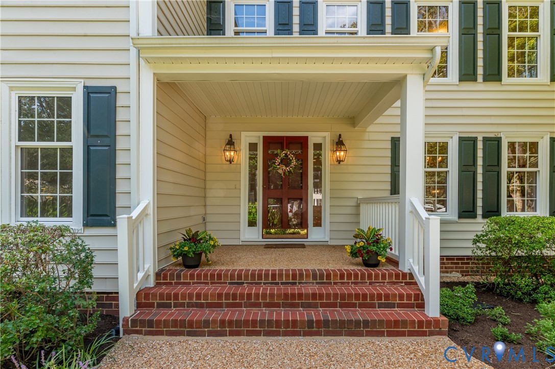 Covered porch entry featuring brick steps, an exposed aggregate landing, and dual decorative sconces Covered porch entry featuring brick steps, an exposed aggregate landing, and dual decorative sconces