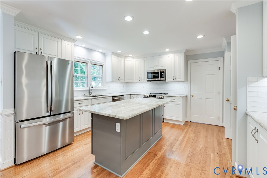 Kitchen featuring light wood-finish flooring, white cabinetry, a center island with a light-toned countertop, stainless steel appliances, and recessed lighting