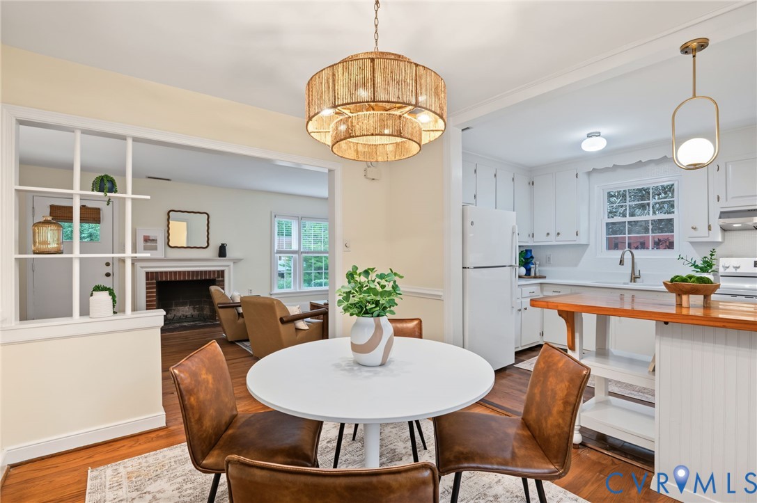 Dining area with a tiered woven chandelier, wood-finish flooring, and an open pass-through to the kitchen featuring white cabinetry and a wood-finish island countertop