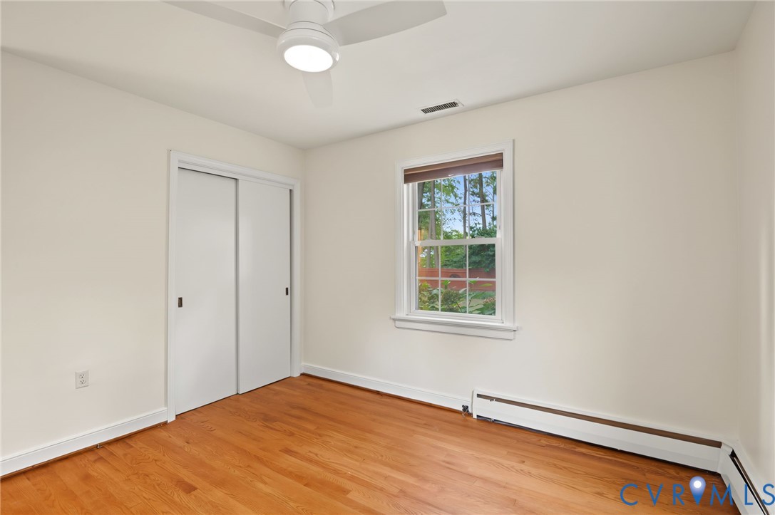 Hardwood flooring, sliding closet doors, single window, ceiling fan, and baseboard heating