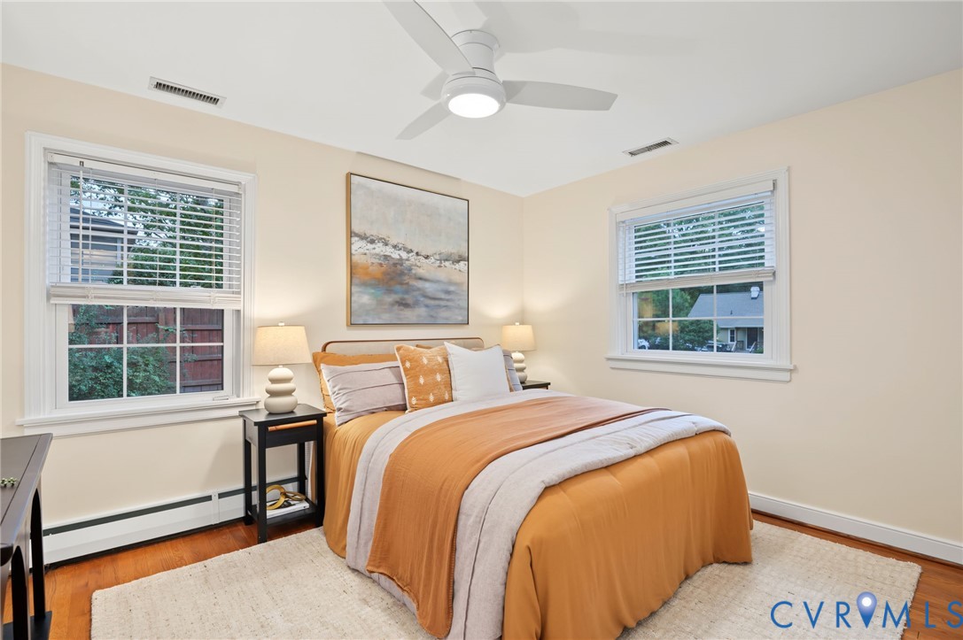 Hardwood-finish flooring, white ceiling fan, and two multi-pane windows with blinds