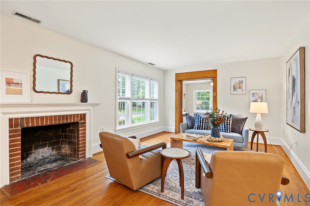 Brick fireplace with a white mantel, wood-finish flooring, white window blinds, and a wood-trimmed doorway Brick fireplace with a white mantel, wood-finish flooring, white window blinds, and a wood-trimmed doorway