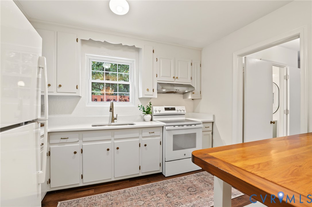 White cabinetry with brass-tone hardware, white countertop surfaces, stainless steel sink with a gooseneck faucet, and wood-finish flooring