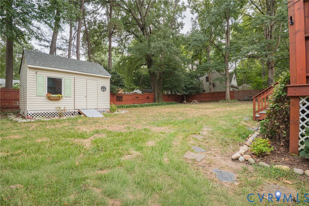 Expansive backyard with a storage shed, wood deck and stairs, and mature trees