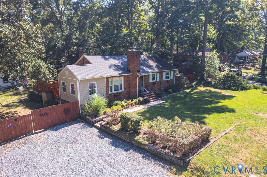 Brick and siding exterior with a shingled roof, gravel driveway, and mature landscaping