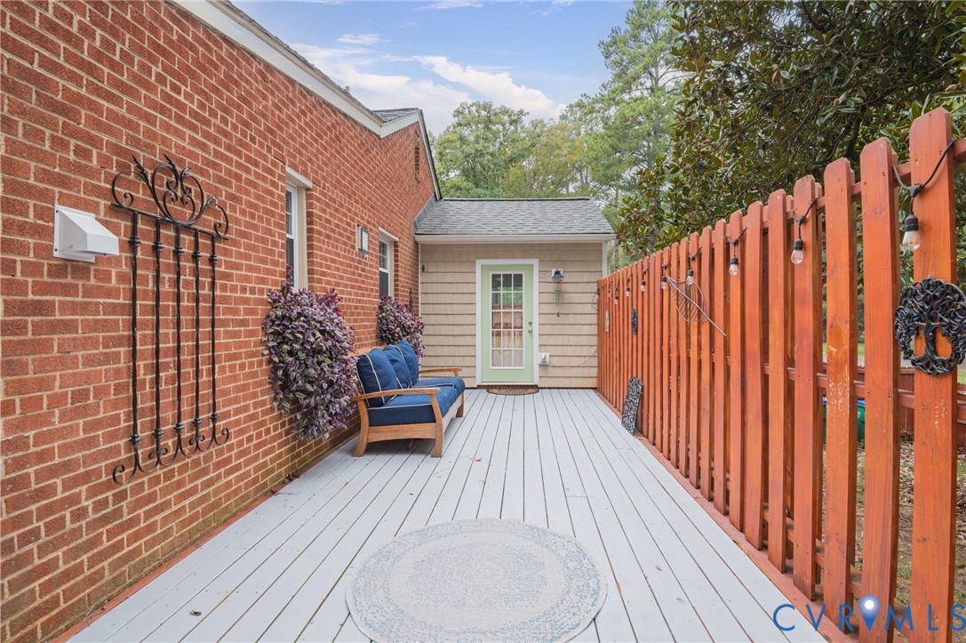 Expansive wood-finish deck with a painted surface, surrounded by a wood fence, and featuring a brick exterior wall