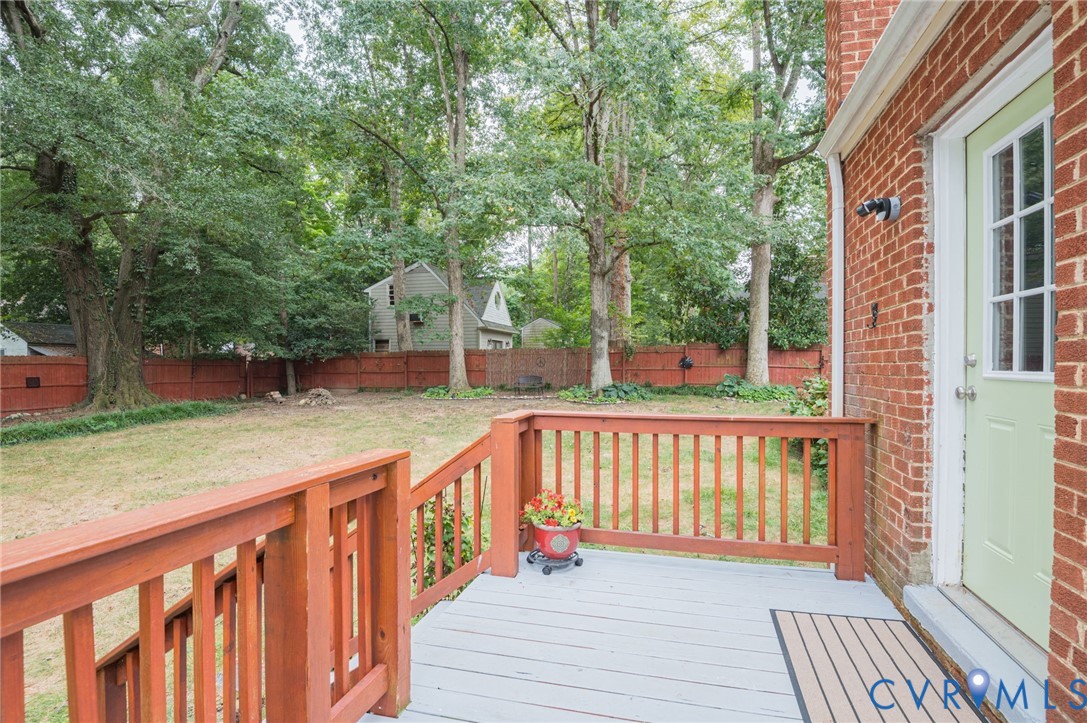 Brick exterior featuring a wood deck with a light-colored finish, wood railings, and a fenced backyard with mature trees