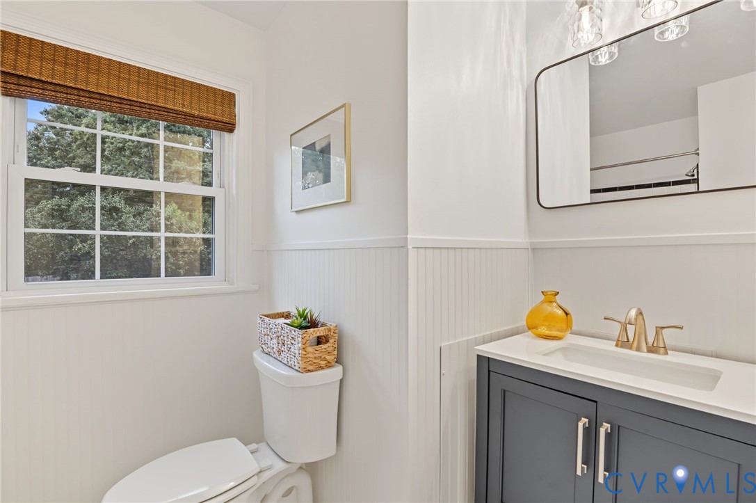 White paneled walls, a white window frame, a dark gray vanity with a white countertop, and a rectangular mirror