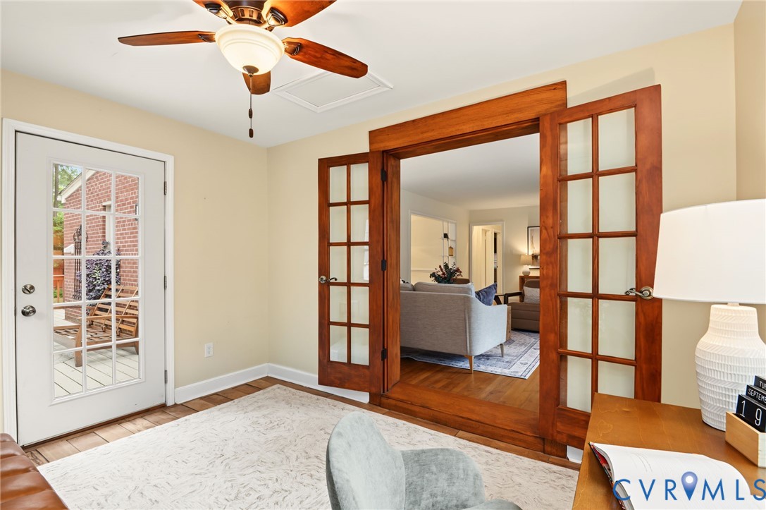 Wood-finish flooring, ceiling fan with integrated lighting, glass-paneled exterior door, and double French doors with wood trim