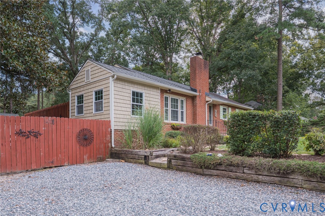 Brick and shake siding exterior with a prominent brick chimney, gravel driveway, and a red wooden fence