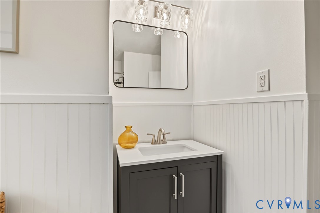 Wall-mounted vanity mirror, modern light fixture, integrated sink, brushed nickel faucet, beadboard wainscoting