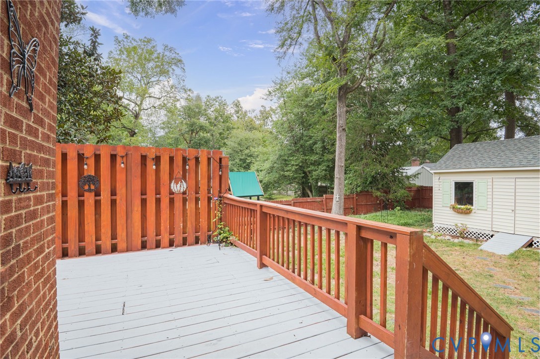 Deck with wood railing and privacy fence, featuring a brick exterior wall and a detached shed with light-colored siding