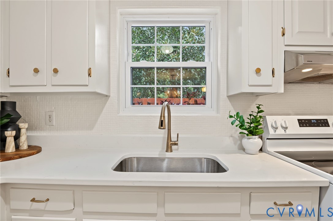 White cabinetry, stainless steel sink, gold-tone faucet, white countertops, and textured white backsplash