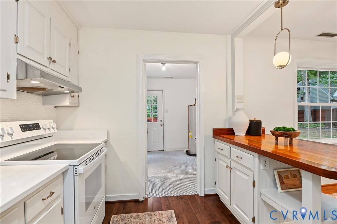 White cabinetry with brass hardware, wood-finish flooring, white solid surface countertops, white electric range with range hood, and a wood-finish bar top with integrated storage