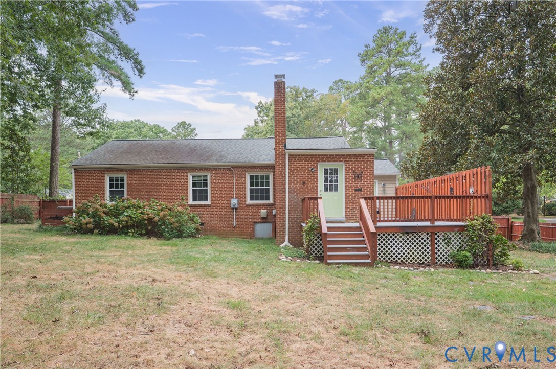 Brick exterior with multiple windows, an exterior chimney, a wooden deck, and a fenced perimeter