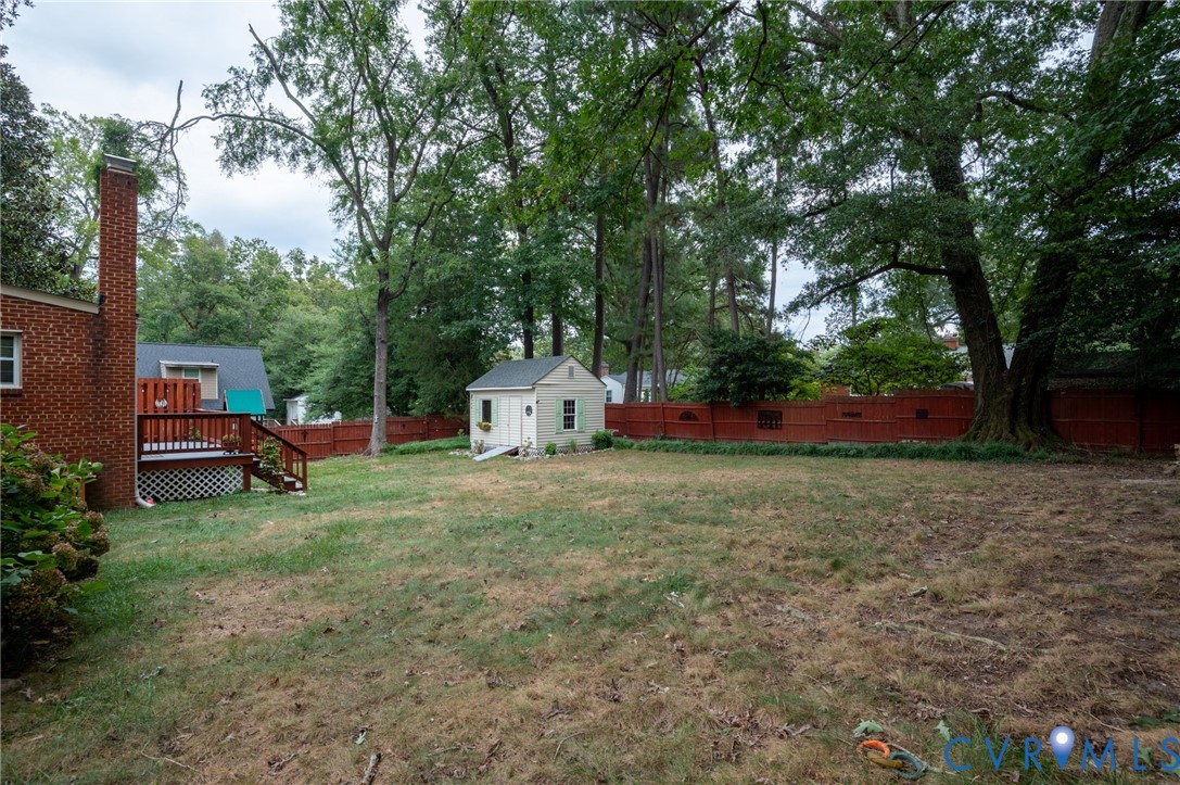 Expansive backyard featuring a red wood-panel fence, mature trees, a detached shed, and a wood deck with lattice skirting