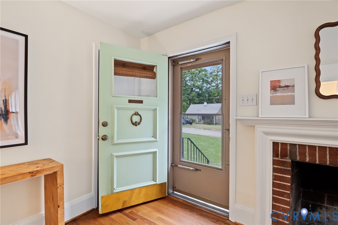 Hardwood flooring, painted interior door, fireplace with brick surround, white mantel, and framed glass storm door