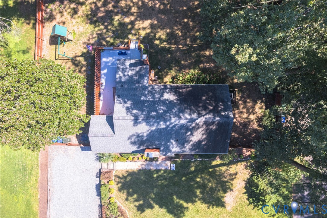 Main residence featuring a gray shingle roof, surrounded by mature trees and a gravel driveway