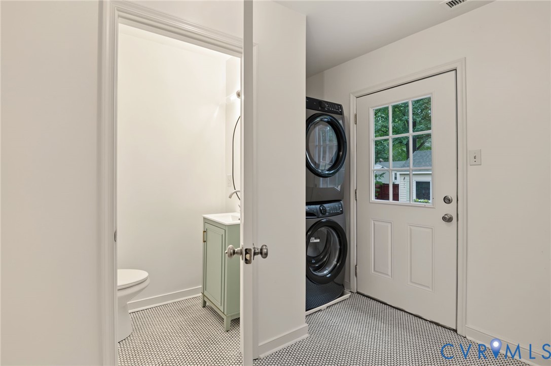 Laundry area with stacked appliances, white paneled door with windowpanes, and tile flooring