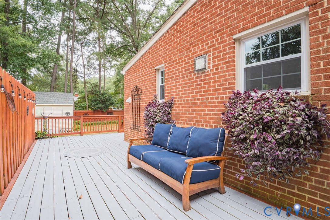 Expansive wood-finish deck with a painted surface, surrounded by a wood fence, and featuring a brick exterior wall