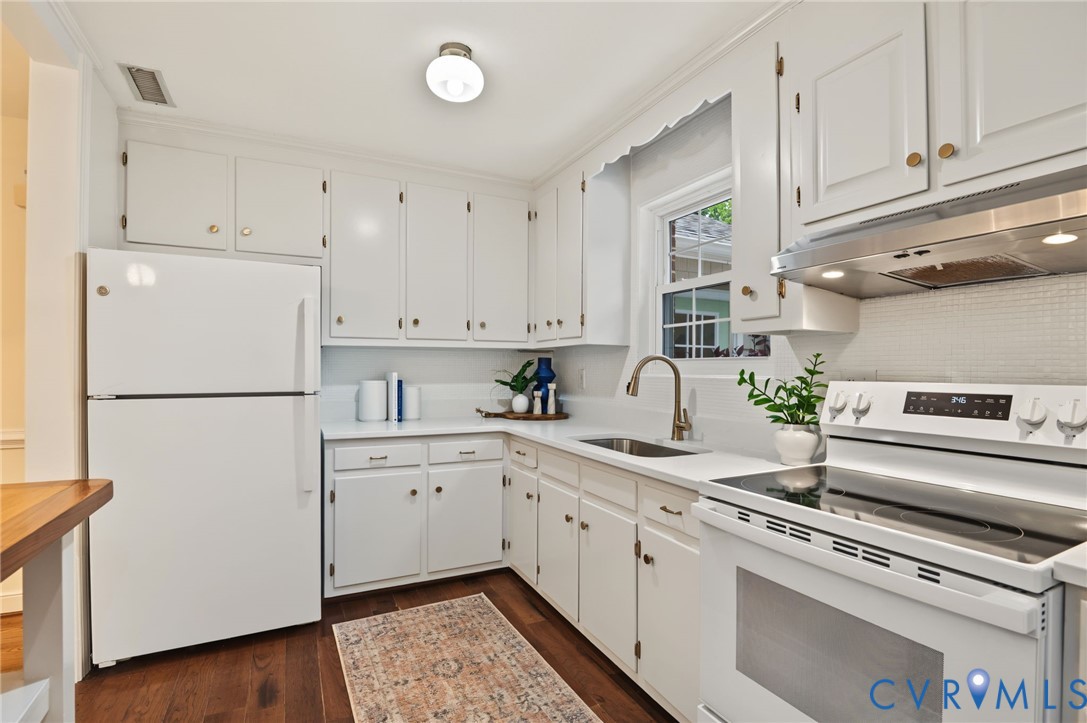 White cabinetry with gold-tone hardware, white countertops, built-in stainless steel range hood, stainless steel sink with gooseneck faucet, and wood-finish flooring
