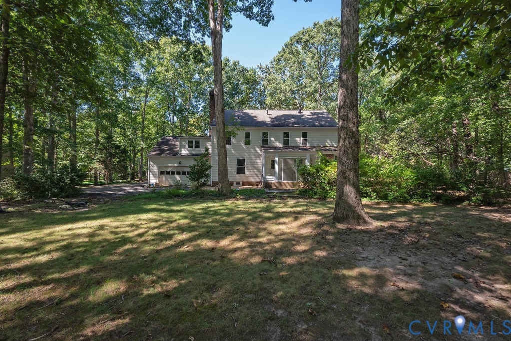 Expansive rear yard with mature trees, a two-story home, attached garage, and screened-in porch