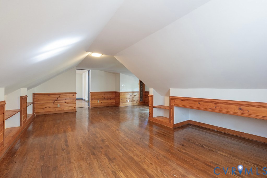 Vaulted ceiling, wood-finish flooring, wood paneling, built-in shelving, and a built-in railing
