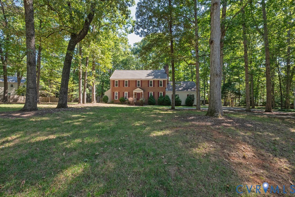 Brick exterior residence with a gabled roof, surrounded by mature trees, set on a grassy lot