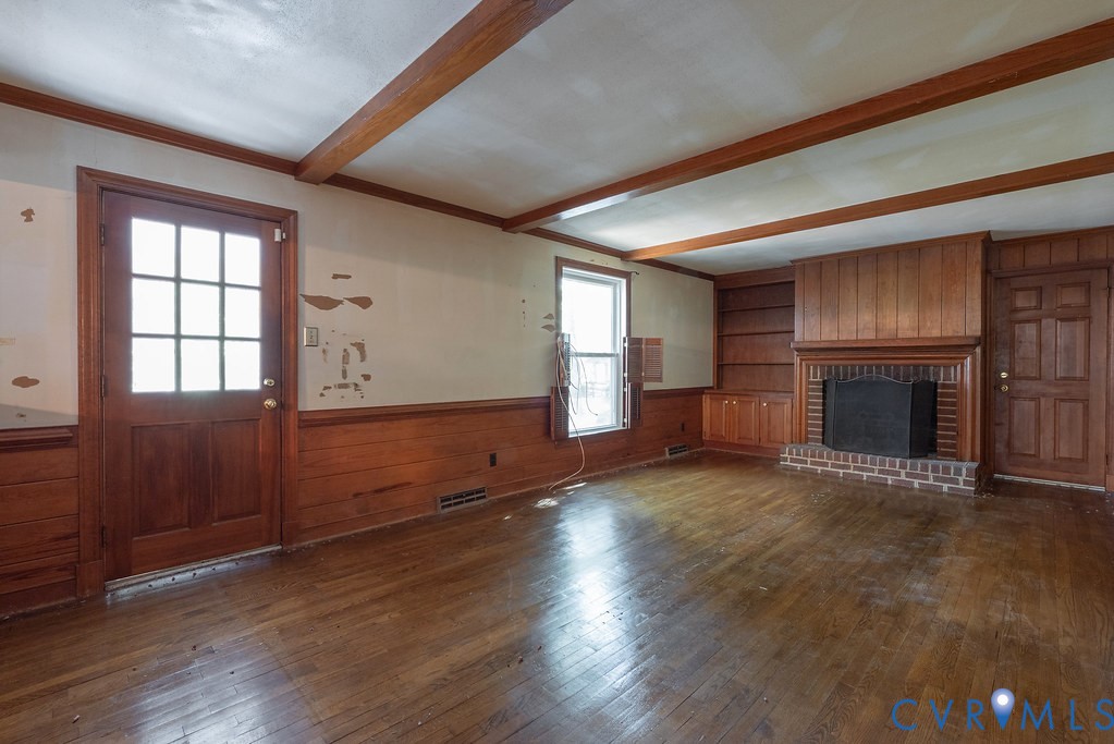 Exposed wood beams, wood-finish flooring, brick fireplace with mantel, built-in shelving, and wainscoting