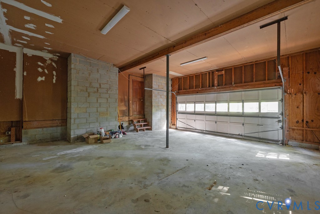 Concrete flooring, exposed block wall, exposed wood framing, overhead fluorescent lighting, and a paneled garage door