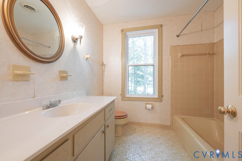 Vanity with integrated sink, coordinating wall sconce, framed mirror, tiled flooring, and a bath/shower combination