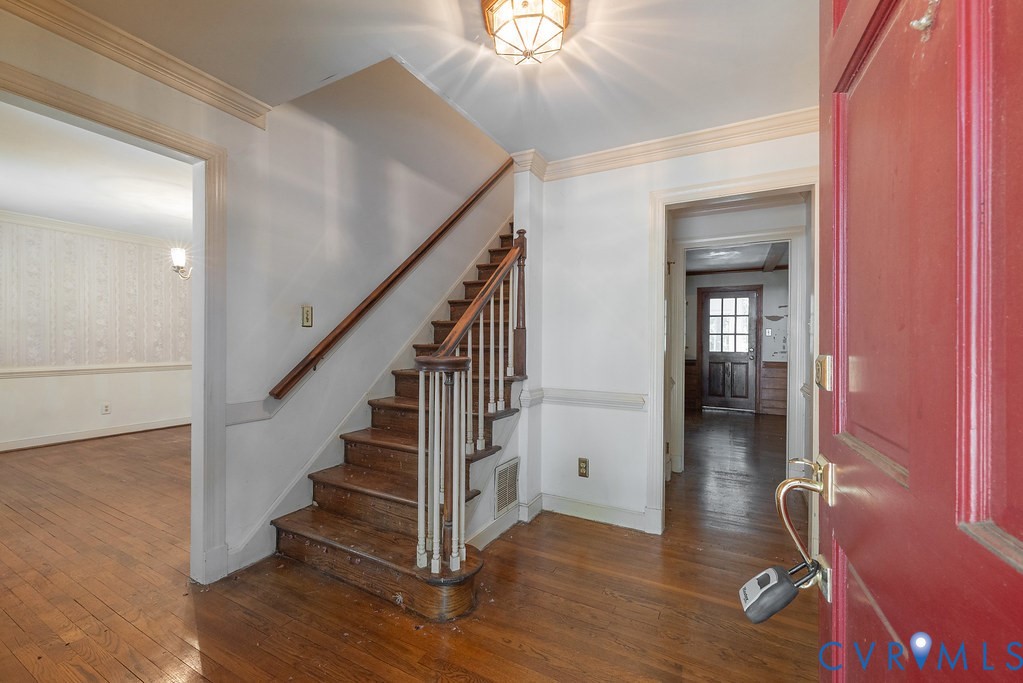 Hardwood flooring, central staircase with wood banister, decorative ceiling light fixture, and crown molding