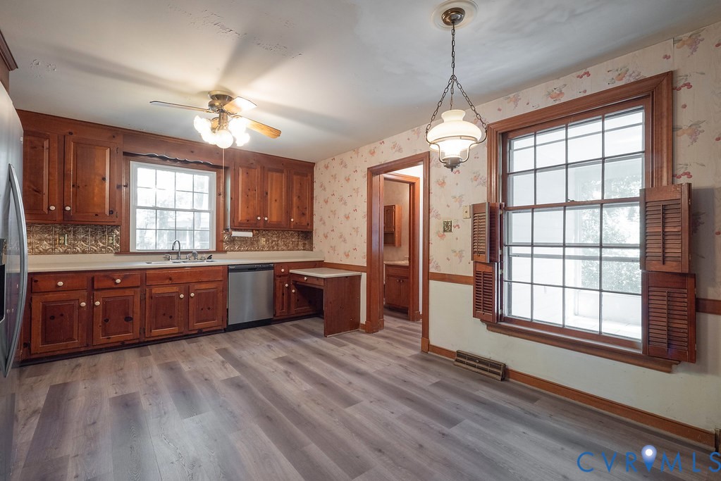 Kitchen featuring wood-finish flooring, wood cabinetry, a stainless steel dishwasher, and a ceiling fan with integrated lighting