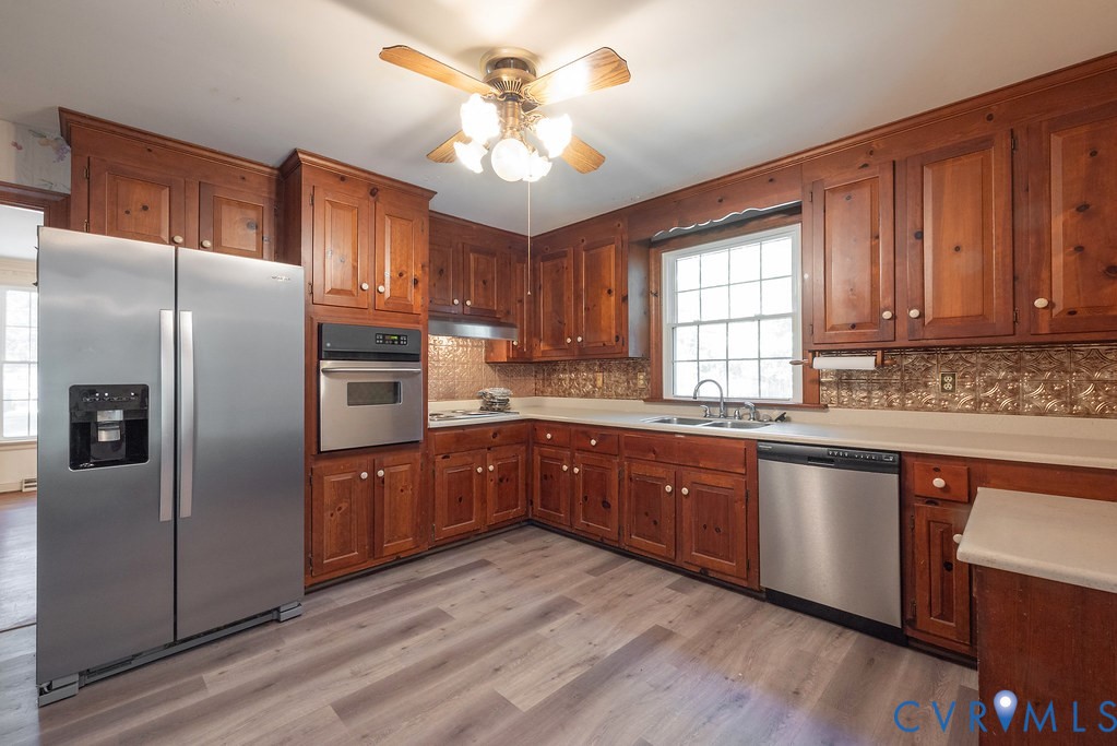 Wood cabinetry, stainless steel appliances, light-toned countertops, and wood-finish flooring