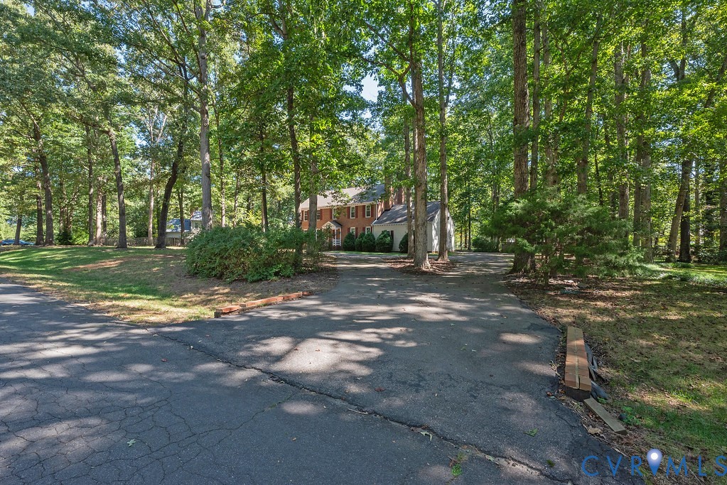 Brick exterior residence with a partial white facade, multi-pane windows, and extensive surrounding mature trees