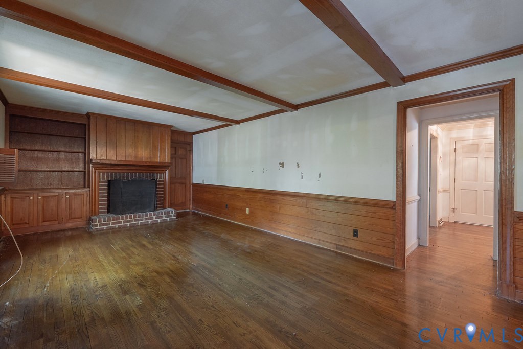 Hardwood flooring throughout, exposed wood ceiling beams, brick fireplace with wood mantel, built-in wood shelving, and wood wainscoting