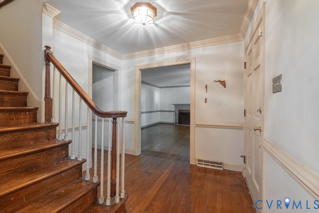 Hardwood flooring, wood staircase with white balusters, crown molding, and wainscoting