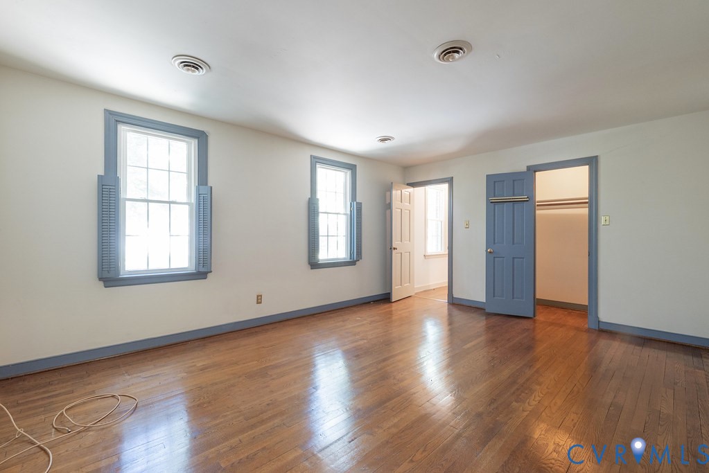 Hardwood-finish flooring, two large windows with shutters, two interior doorways, and an open closet with hanging rods