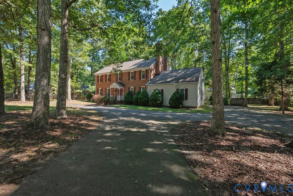 Traditional brick residence featuring a portico entry, white siding accent, and red window shutters
