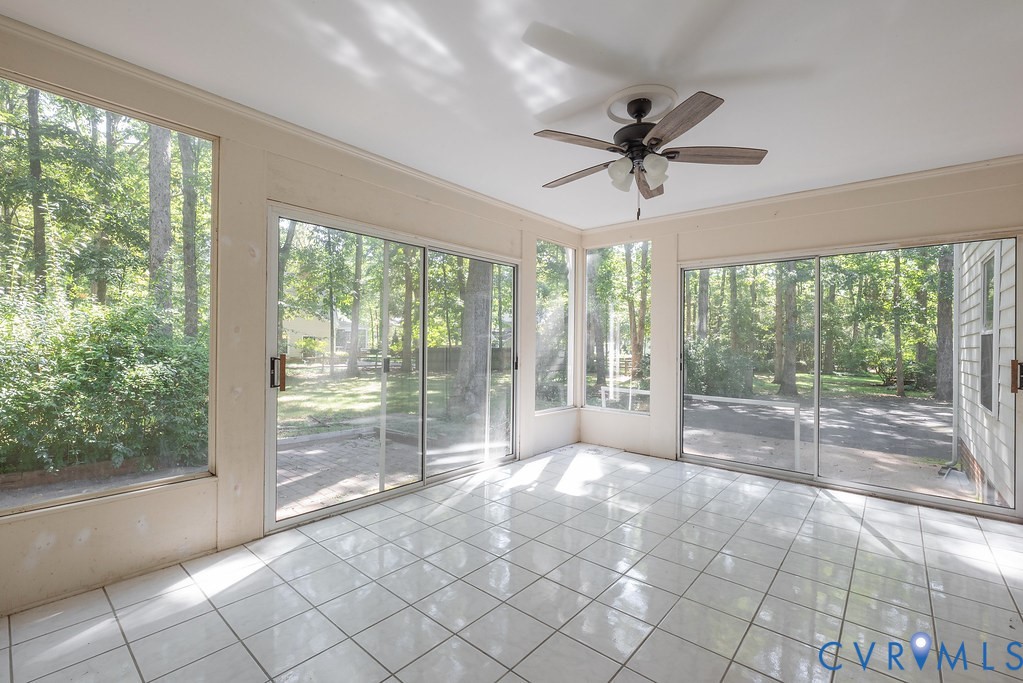 Expansive sunroom featuring multiple sliding glass doors, large fixed windows, tiled flooring, and an overhead ceiling fan with integrated lighting