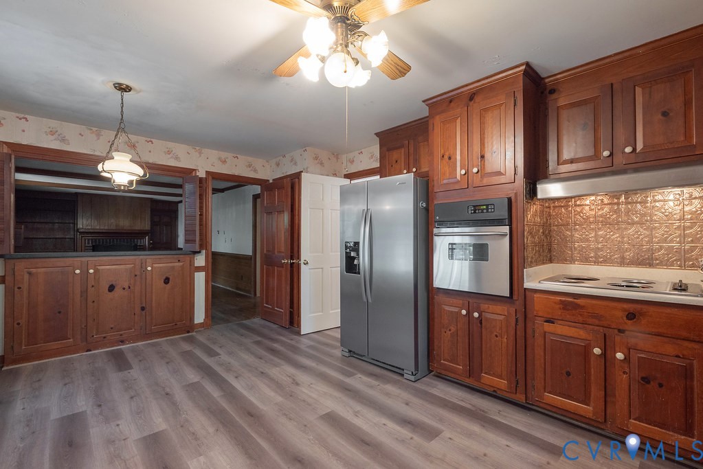 Wood-finish flooring, wood cabinetry, stainless steel appliances, built-in oven, and a decorative backsplash