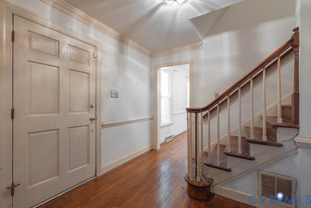 Entryway featuring wood-finish flooring, a paneled door, and a staircase with a wood handrail