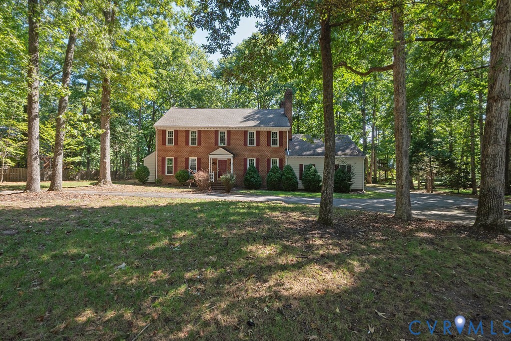 Brick colonial residence featuring red shutters, a columned portico, and mature trees