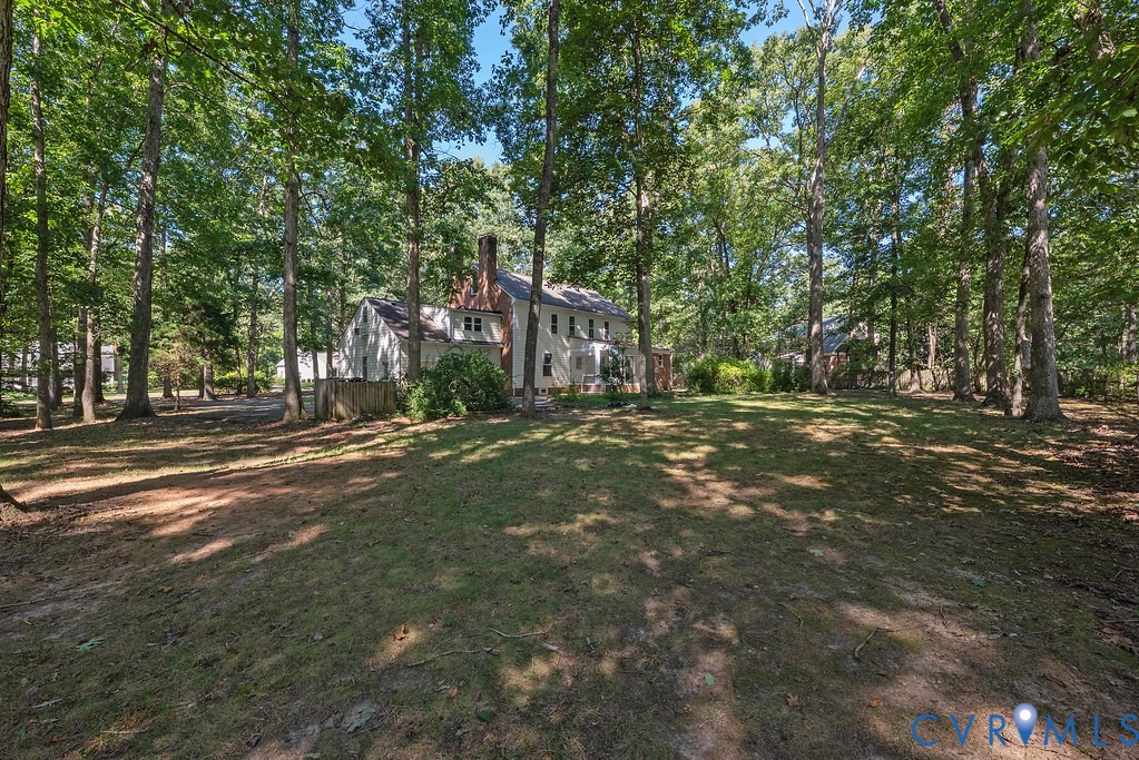 Expansive rear yard featuring mature trees, a manicured lawn, and a light-colored siding exterior with a brick chimney