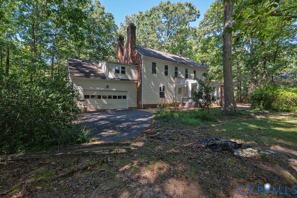 Two-story siding exterior with multiple windows, attached two-car garage, and prominent brick chimney