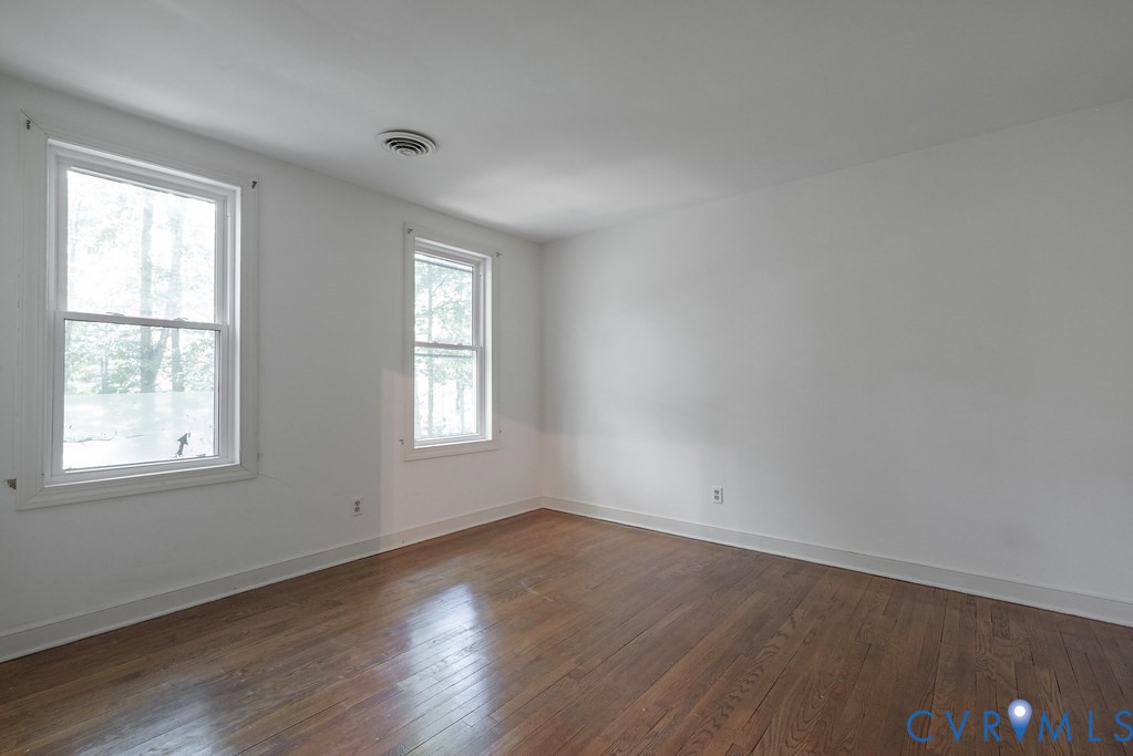 Hardwood flooring, two single-hung windows with white trim, white walls, and a ceiling-mounted circular vent