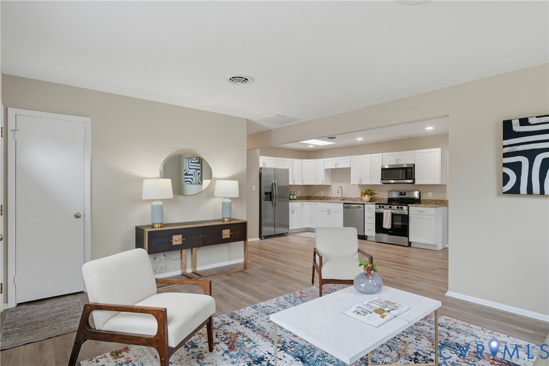 Open-concept living space with wood-finish flooring, recessed lighting, and a white kitchen featuring stainless steel appliances and light-toned countertops