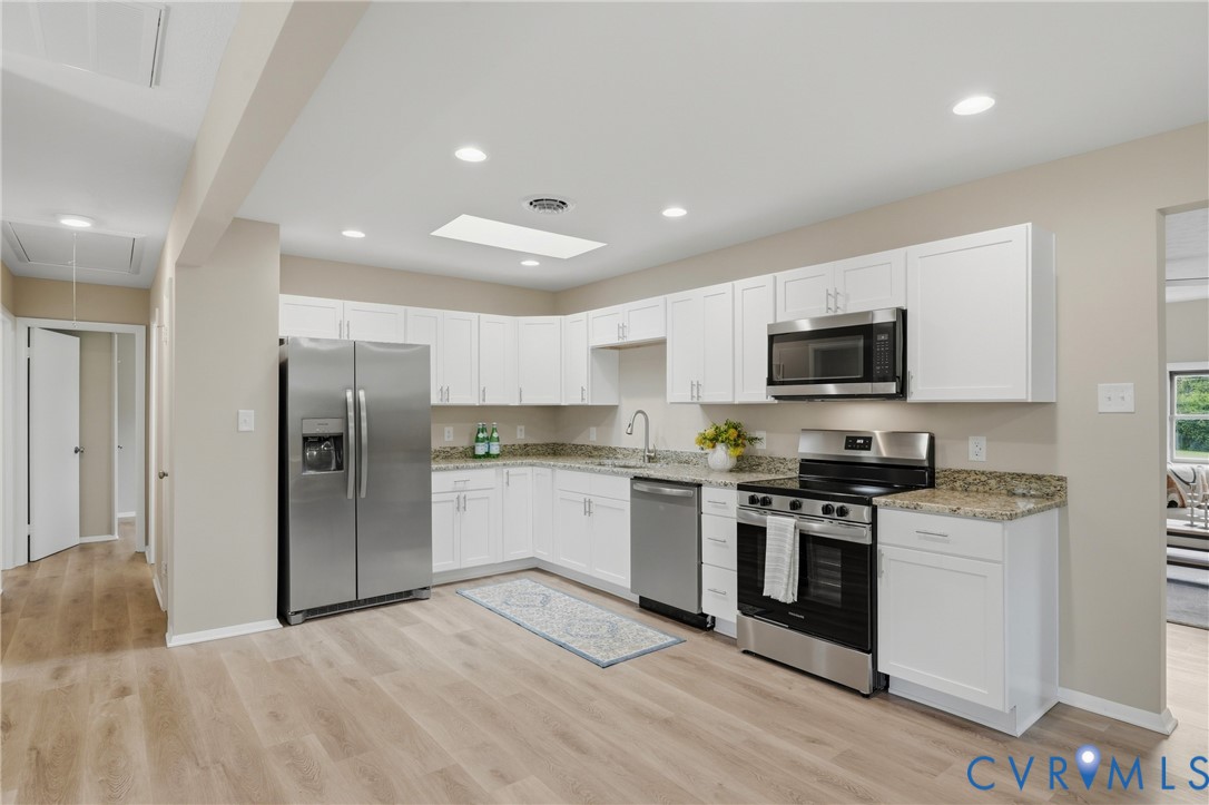 Kitchen featuring white cabinetry, stainless steel appliances, speckled stone countertops, and wood-finish flooring