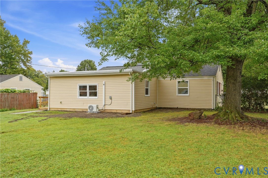 Expansive lawn area, mature trees, tan siding, multiple windows, and a wood privacy fence